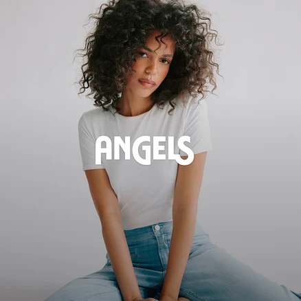 Žena s kučeravými vlasmi v bielom tričku a svetlomodrých džínsoch sedí a pozerá sa do kamery. Na obrázku je prekrytý nápis ANGELS.