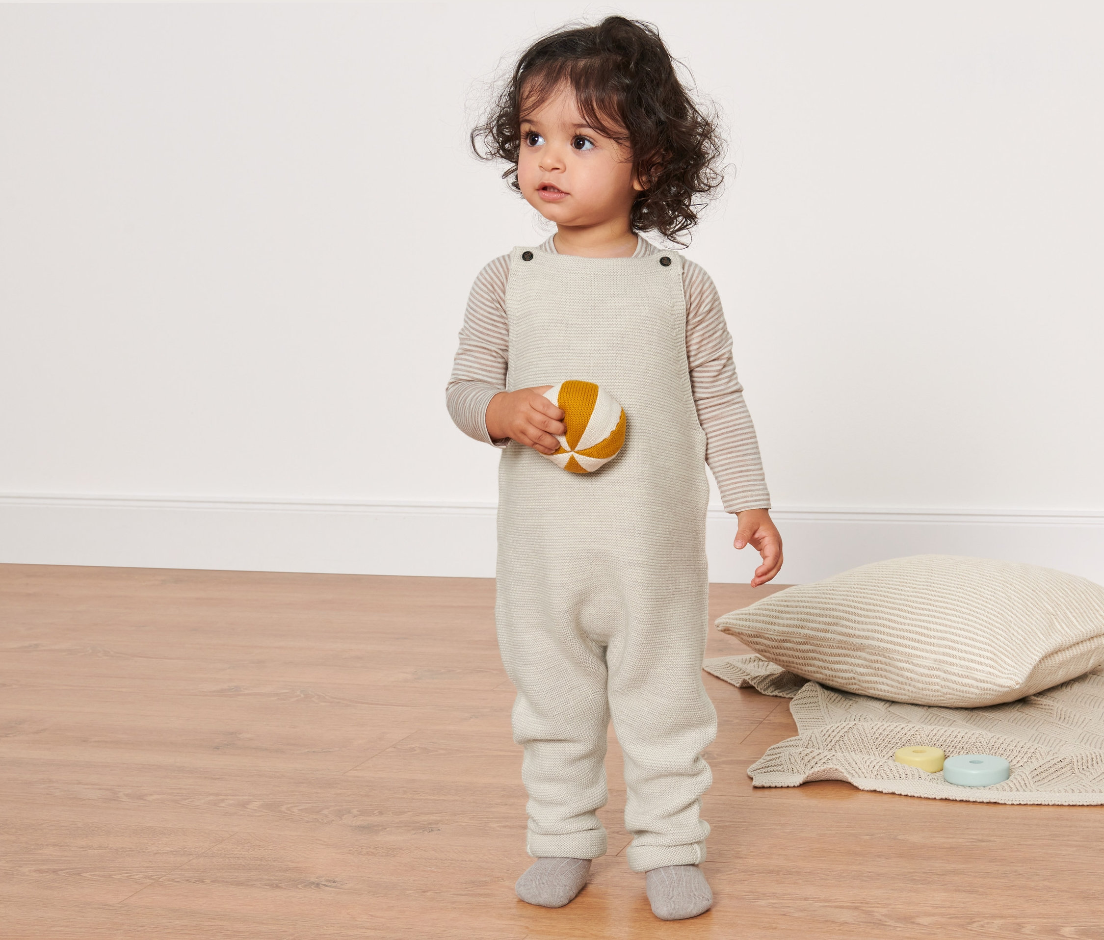 Dieťa drží loptu a má na sebe nohavice s náprsenkou z vlny s certifikátom RWS.