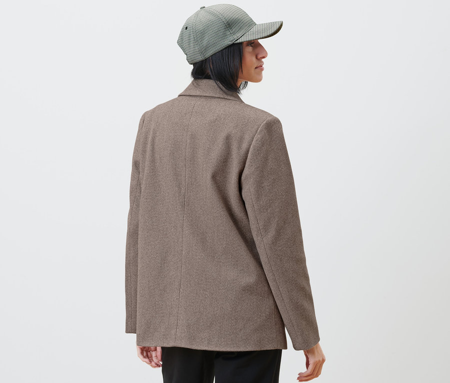 Žena v saku a kockovanej čiapke sa pozerá doprava.