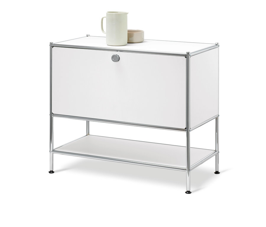 Biela odkladacia skrinka »CN3« s jednými výklopnými dvierkami. Na vrchnej doske stojí keramický džbán a miska.