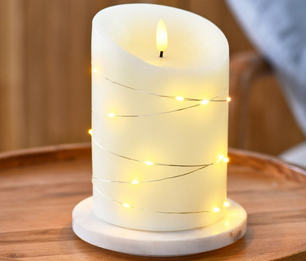 LED sviečka z pravého vosku s reťazou s mikrosvetielkami stojí na okrúhlom drevenom stolíku.