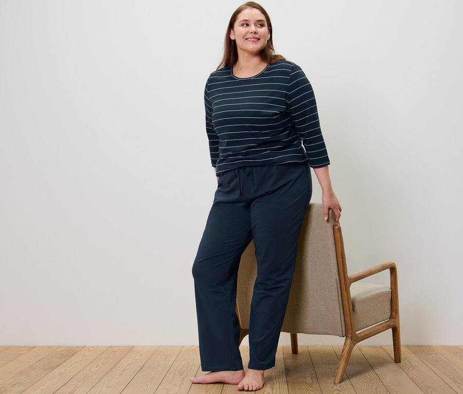 Žena v tmavomodrom pruhovanom pyžame stojí vedľa kresla.