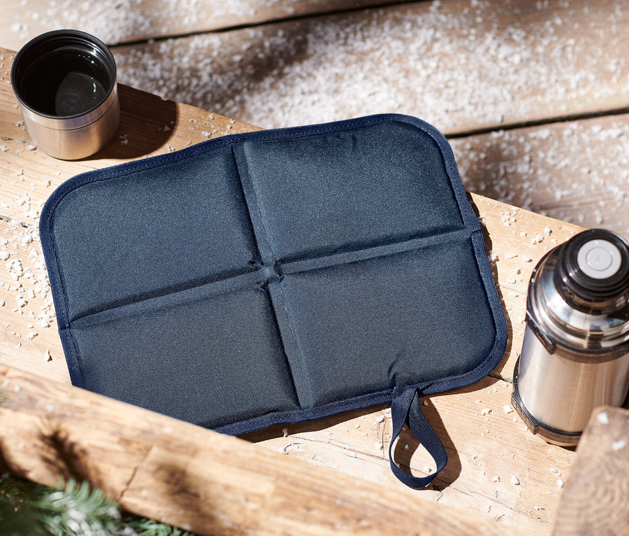 Skladací termovankúš na sedenie a termoska na drevenom stole.