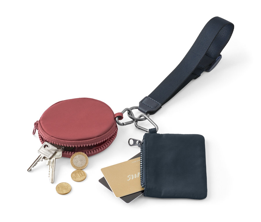 Vínová okrúhla peňaženka s kľúčmi a mincami vedľa modrej peňaženky na zips s kartami a multifunkčnou kľúčenkou.