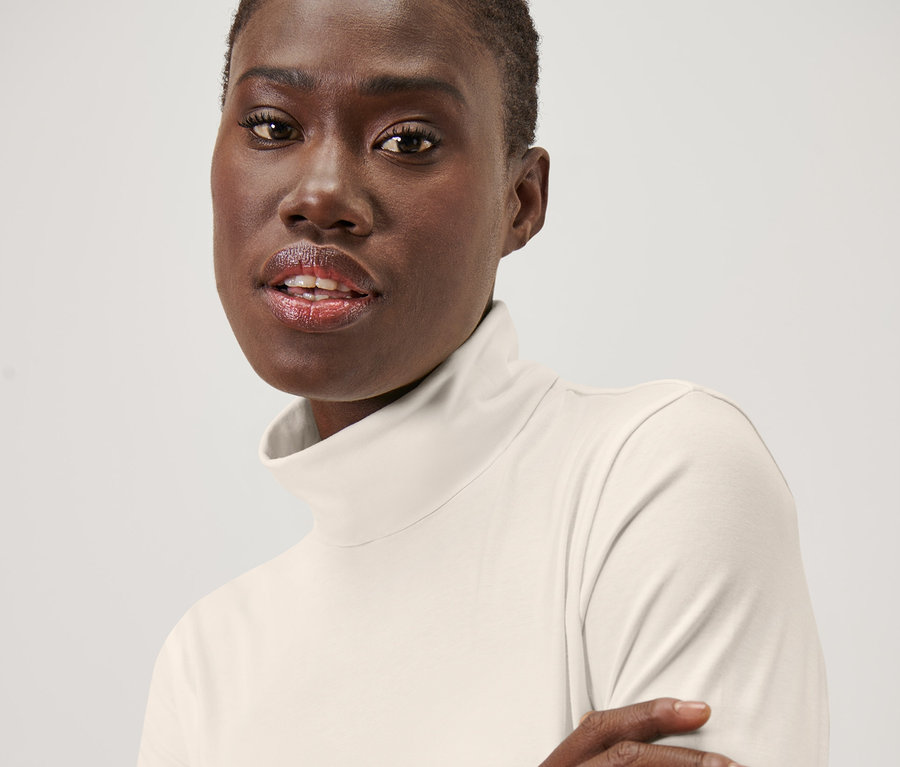 Portrét ženy v krémovobielom rolákovom tričku.