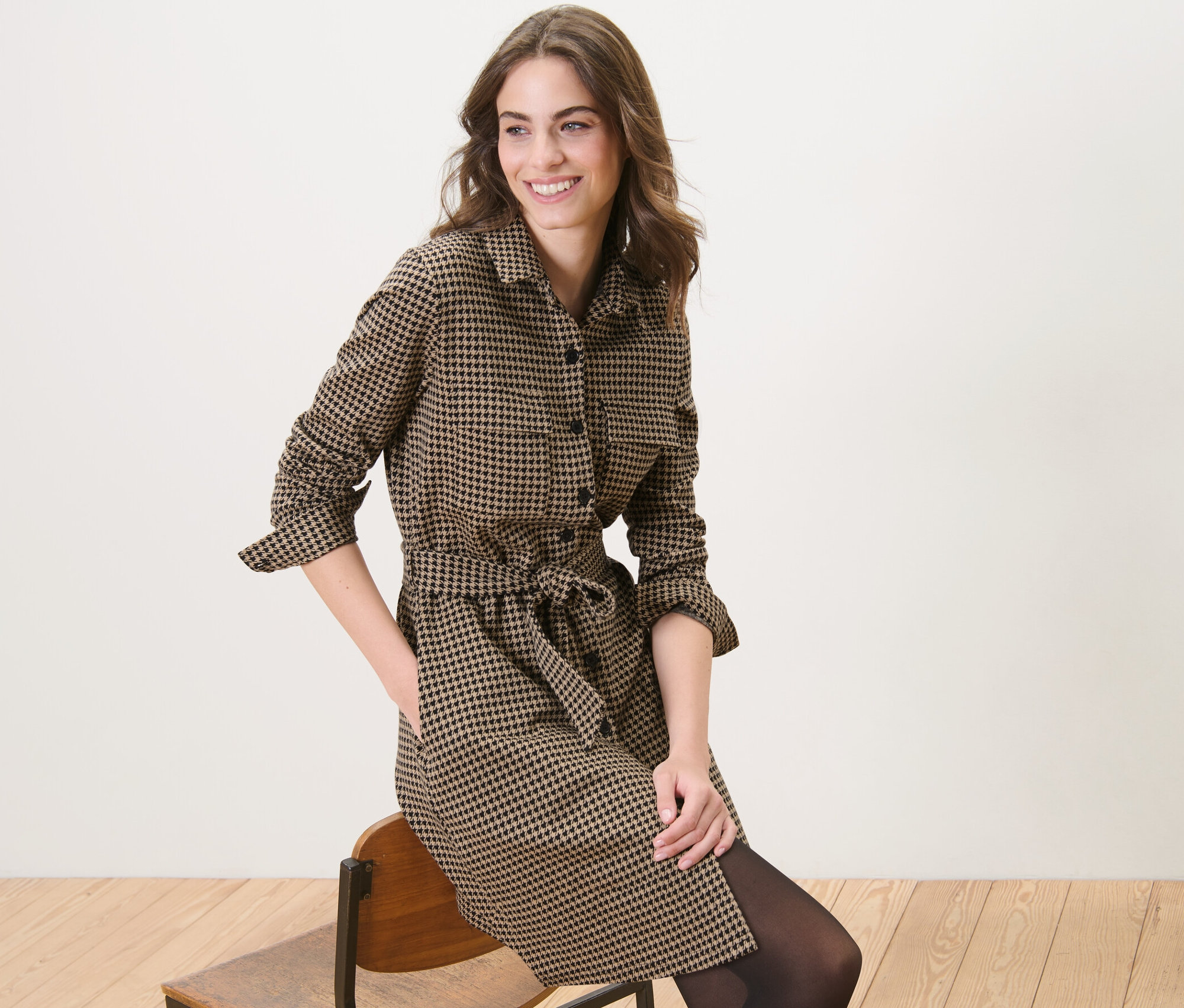 Žena sedí na stoličke a má na sebe teplákové šaty so žakárovým vzorom kohútej stopy.