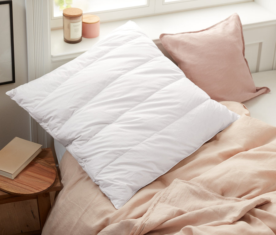 Na posteli ležia biely prešívaný vankúš a ružový vankúš vedľa vankúša s výplňou z limbového dreva.