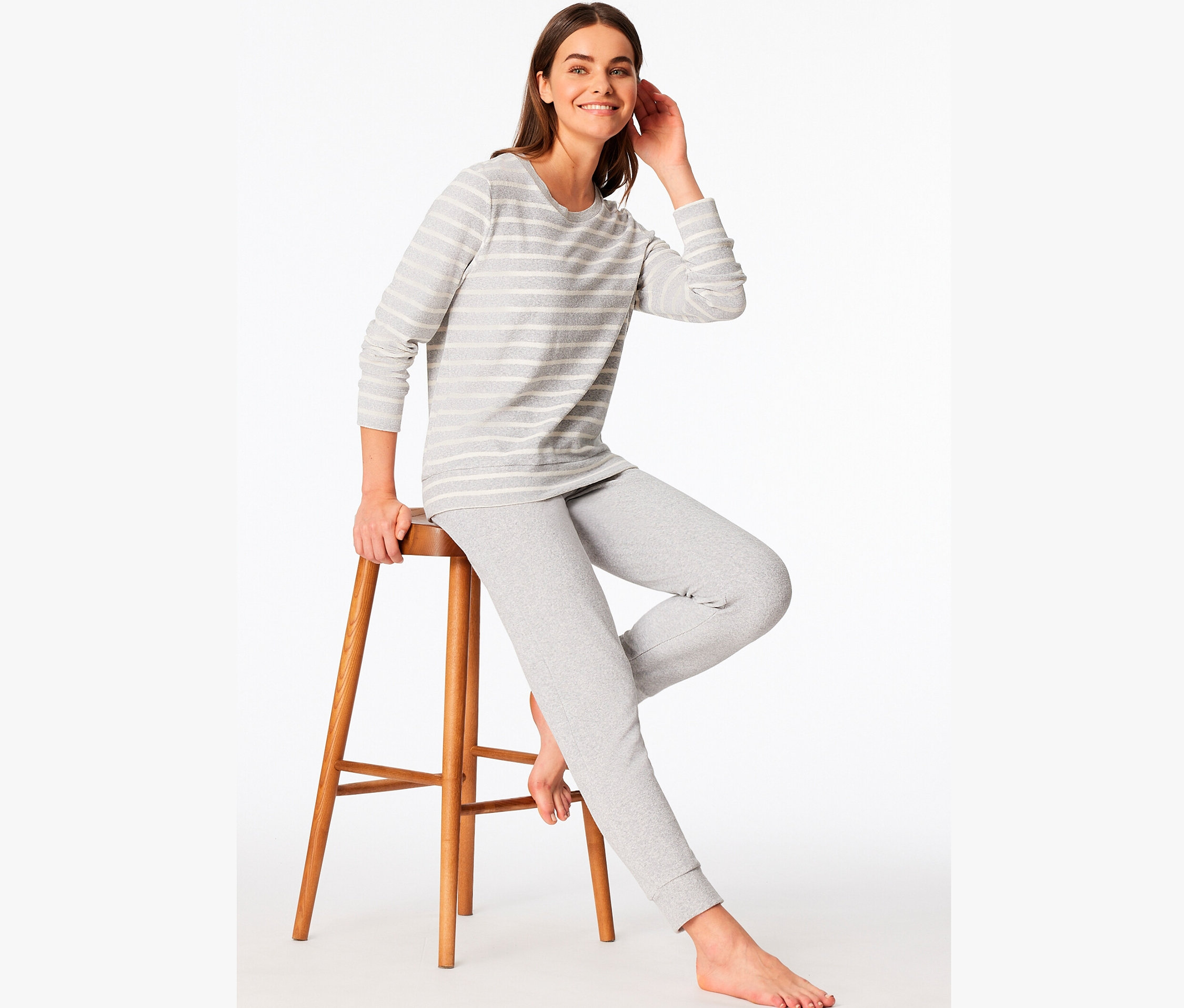 Žena sedí na drevenej stoličke a má na sebe sivé pruhované pyžamo.