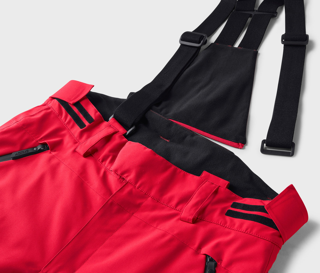 Detail červených lyžiarskych nohavíc s čiernymi traky.
