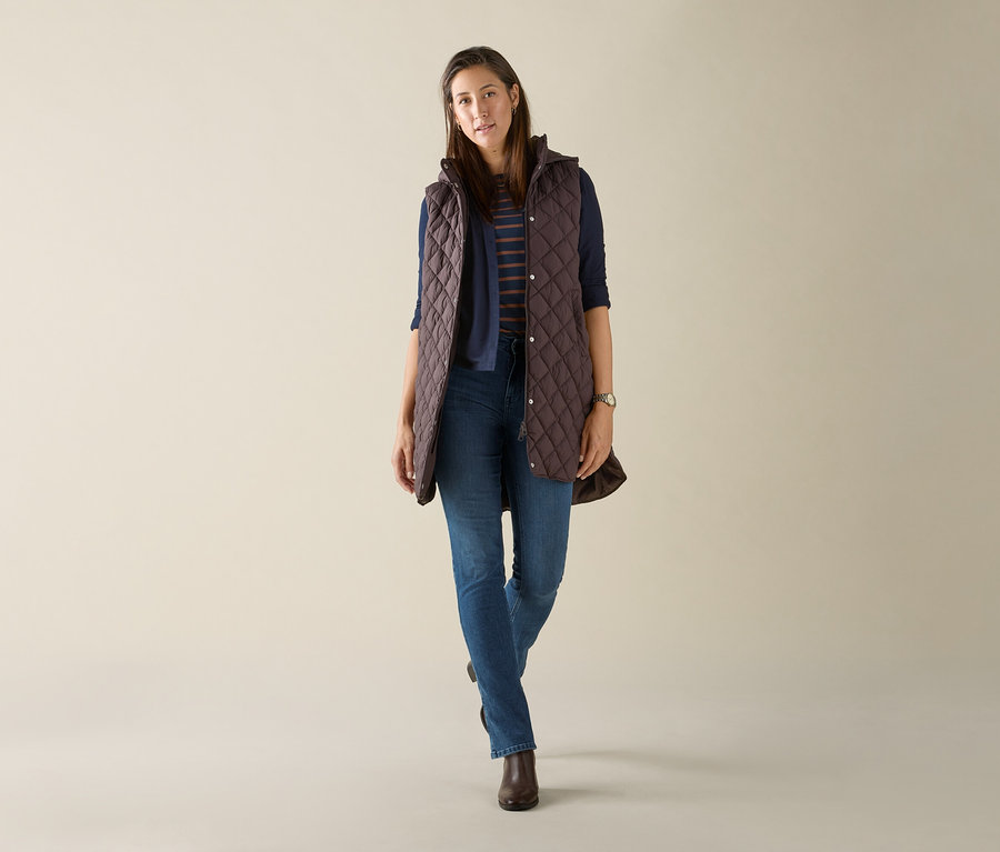 Žena má na sebe dlhú prešívanú vestu s kapucňou tmavohnedej farby.