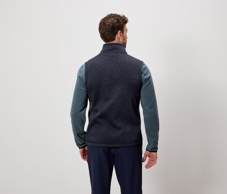 Muž chrbtom k fotoaparátu má na sebe tmavomodrú vestu a modrý sveter.