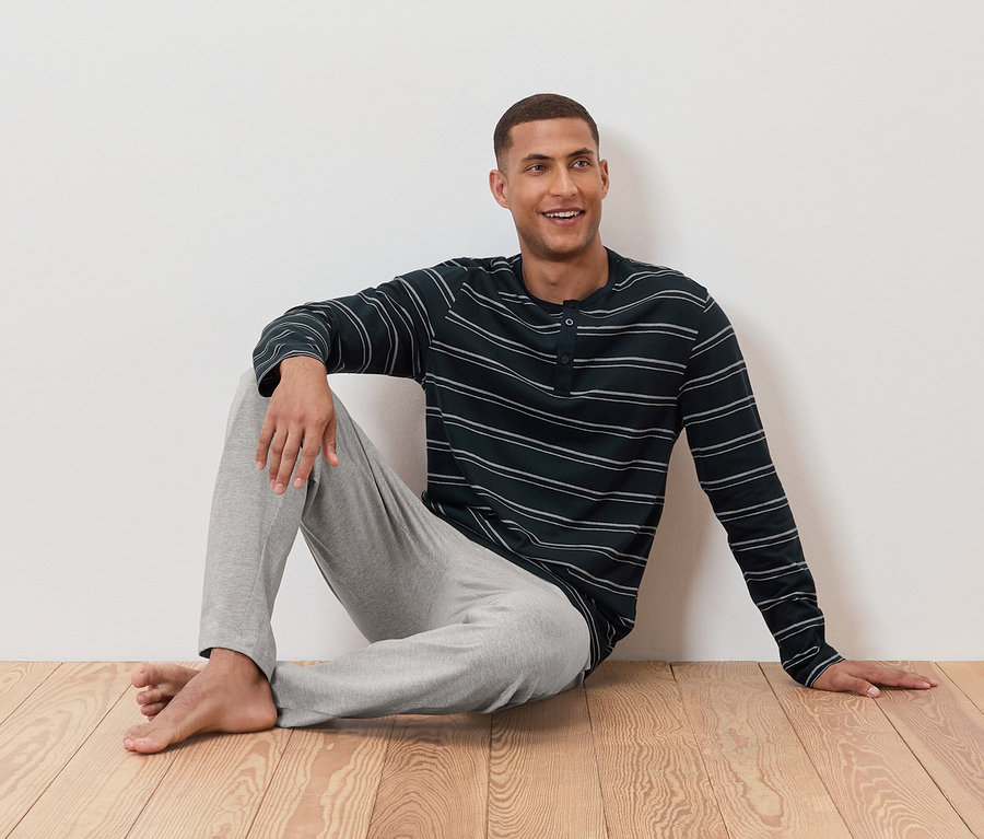 Muž sedí na podlahe v pruhovanom pyžame a sivých nohaviciach.