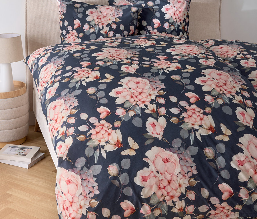 Posteľ s kvetinovou posteľnou bielizňou a nočný stolík s lampou.