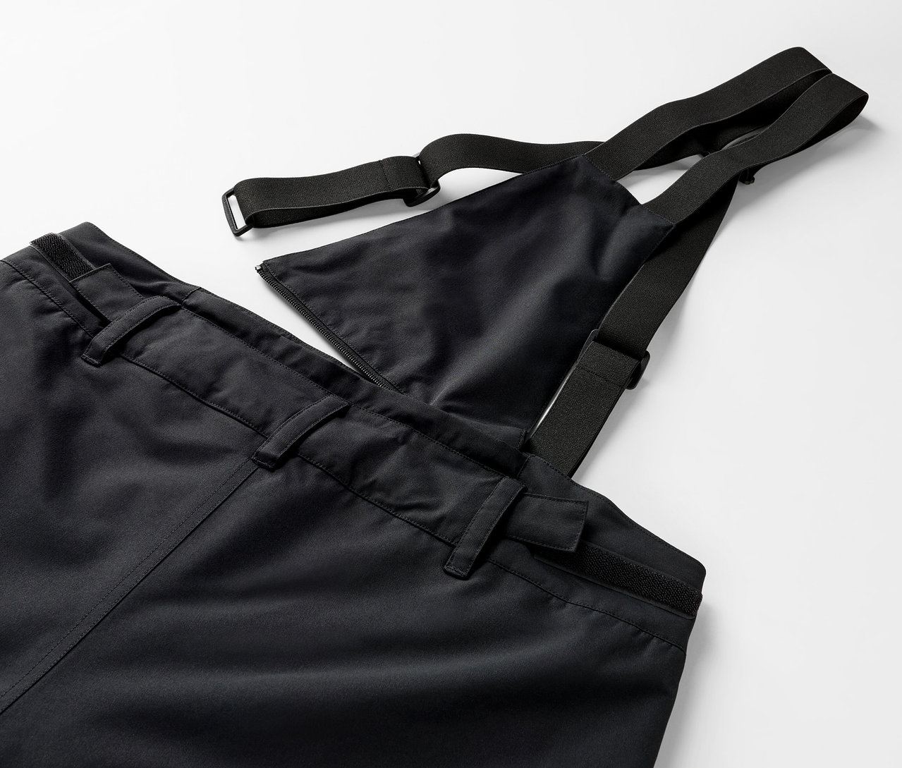 Detail čiernych nohavíc s náprsenkou a elastickými popruhmi.