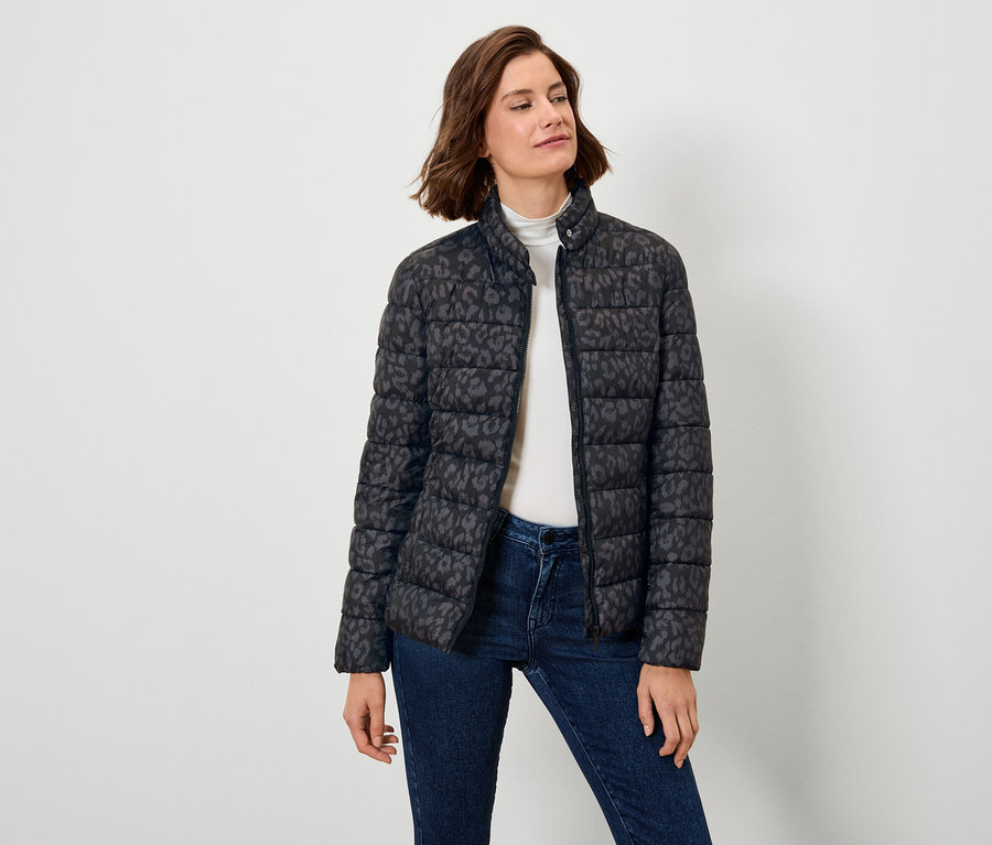 Žena má na sebe čiernu páperovú bundu s potlačou a džínsy.