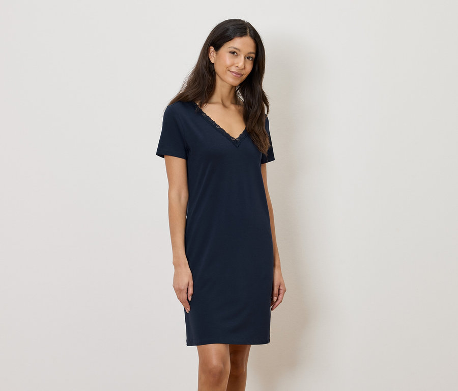 Žena má na sebe tmavomodré šaty po kolená s čipkovaným lemom na výstrihu do V.