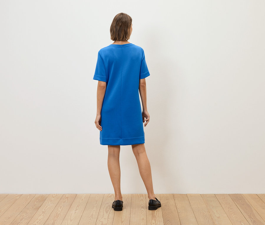 Žena chrbtom k fotoaparátu má na sebe modré šaty a čierne topánky.