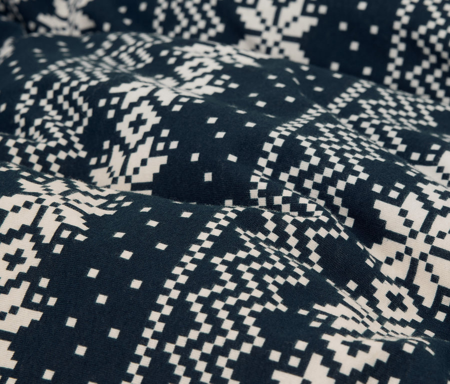 Detailný záber na látku s pixelovým dizajnom snehových vločiek v tmavomodrej a bielej farbe.