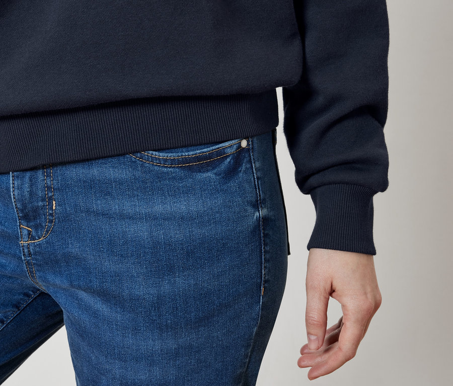 Detail modrých džínsov a tmavomodrej mikiny na tele osoby.