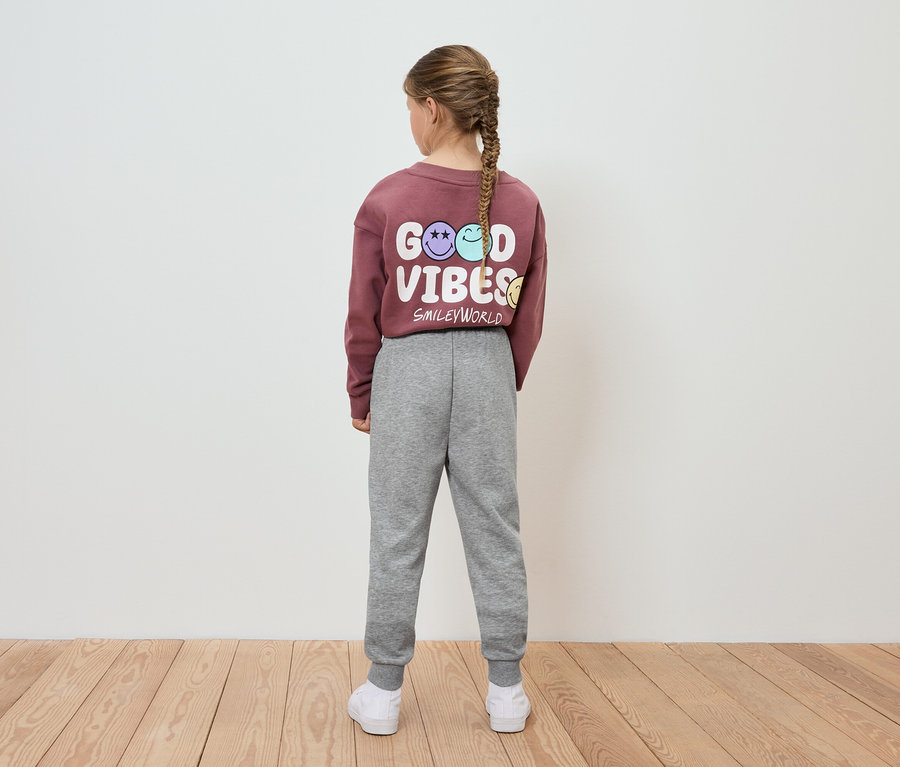 Dievča v bordovej mikine s nápisom Good Vibes a sivých teplákoch stojí chrbtom k fotoaparátu.