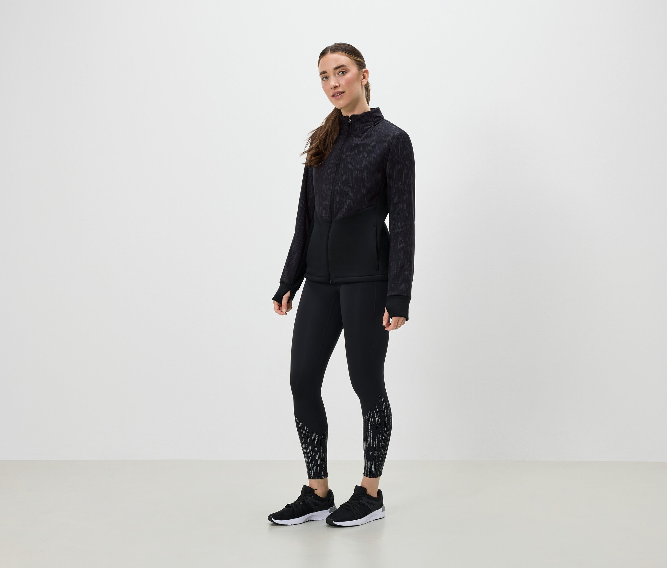 Žena v čiernom športovom oblečení pózuje na svetlom pozadí.