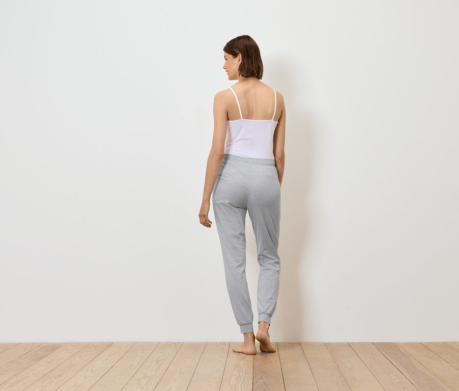 Žena stojí chrbtom, má na sebe biely top a sivé tepláky.