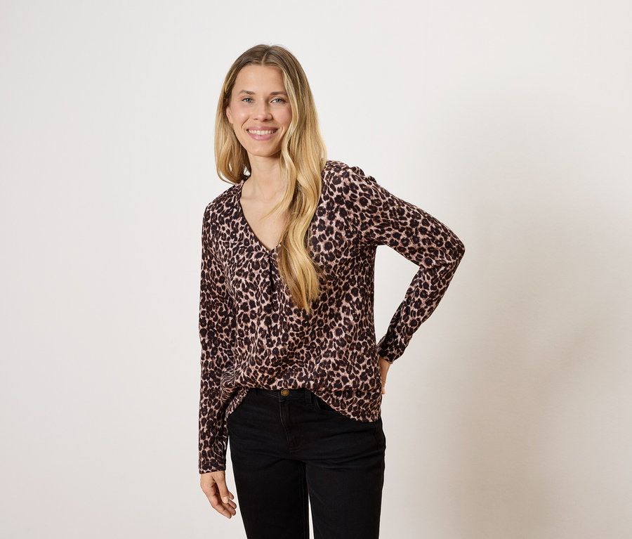 Žena s dlhými blond vlasmi pózuje v blúzke so zvieracím vzorom a čiernych nohaviciach.