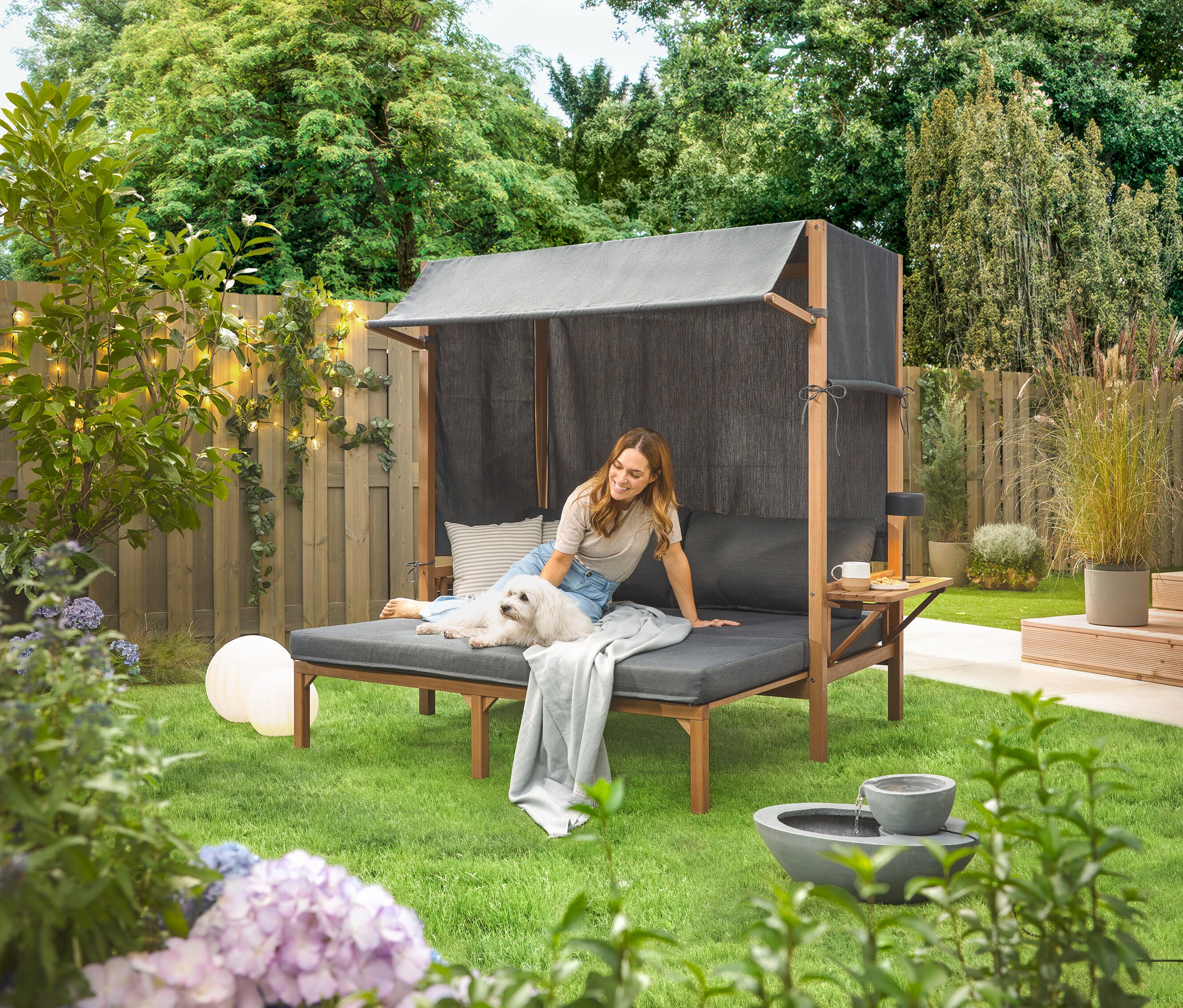 Žena sedí so psom na solárnej záhradnej fontáne v záhrade.