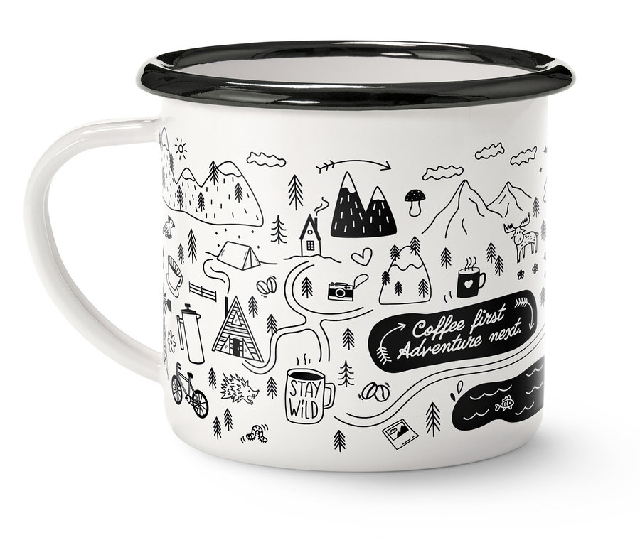 Biely hrnček s čiernym okrajom a rúčkou, zdobený kresbou hôr, stromov a nápisom "Coffee first, Adventure next".