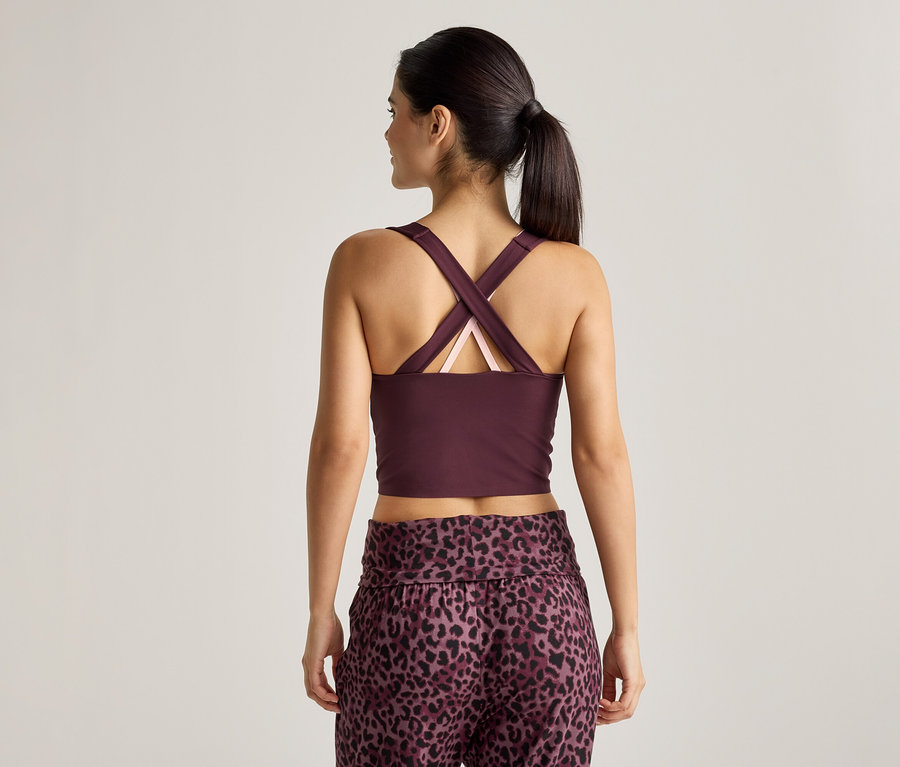 Pohľad zozadu na ženu s copom, ktorá má na sebe vínový crop top so skríženými ramienkami a nohavice s leopardím vzorom.