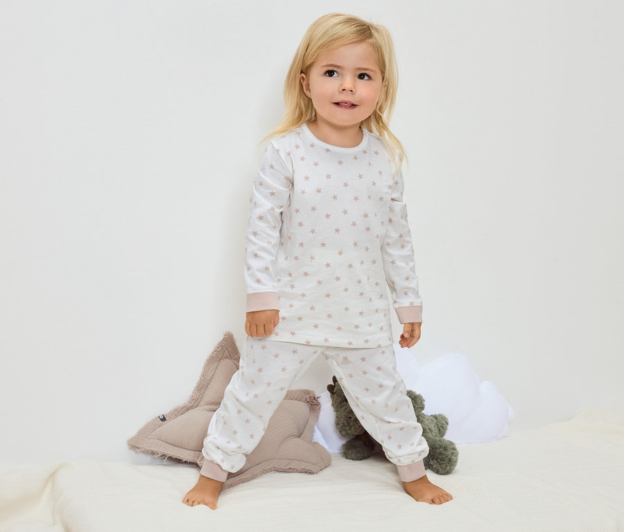 Malé blond dievča stojí bosé na deke a má na sebe biele pyžamo s hviezdami.