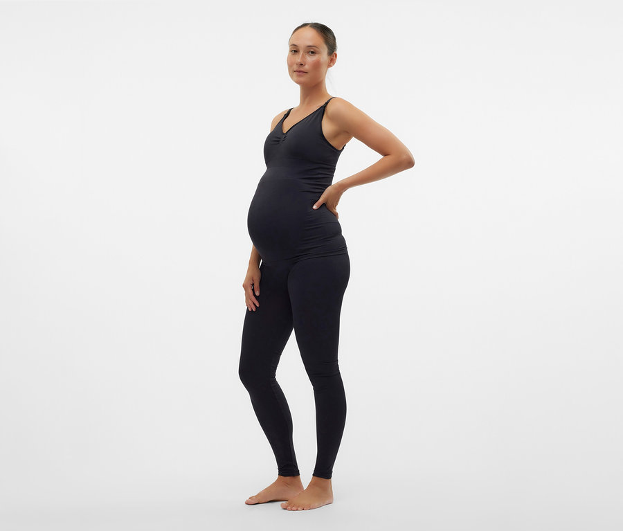 Tehotná žena v čiernom tope a skinny legínach MAMALICIOUS »MLTIA JEANNE« pózuje zboku.