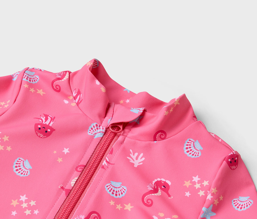 Detailný záber na ružové plavky na zips so vzorom morských koníkov, mušlí a hviezd.