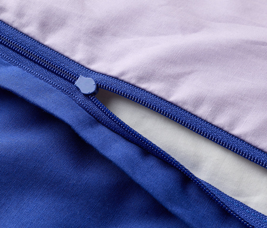 Detailný záber na čiastočne otvorený zips na fialovej a modrej látke.