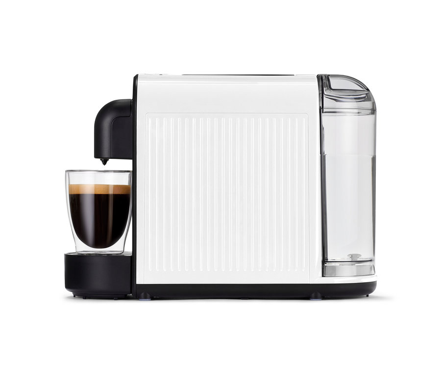 Biely kávovar Cafissimo now white so šálkou plnou kávy stojí na stole.