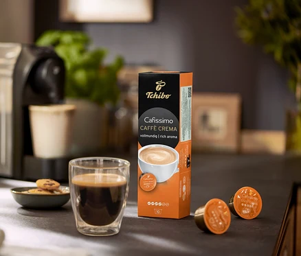 Kávovar so šálkou kávy, sušienkami a balením kapsúl Cafissimo Caffe Crema.