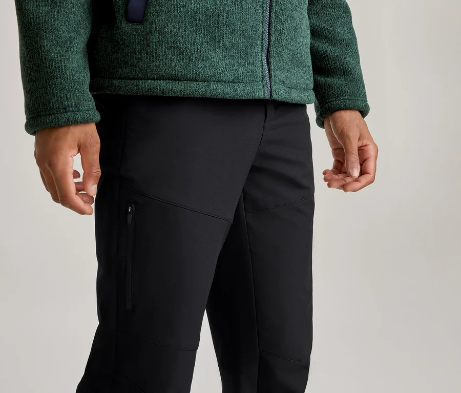 Osoba v zelenej textúrovanej flísovej bunde so zipsom a čiernych nohaviciach s vreckom na zips na ľavom stehne.