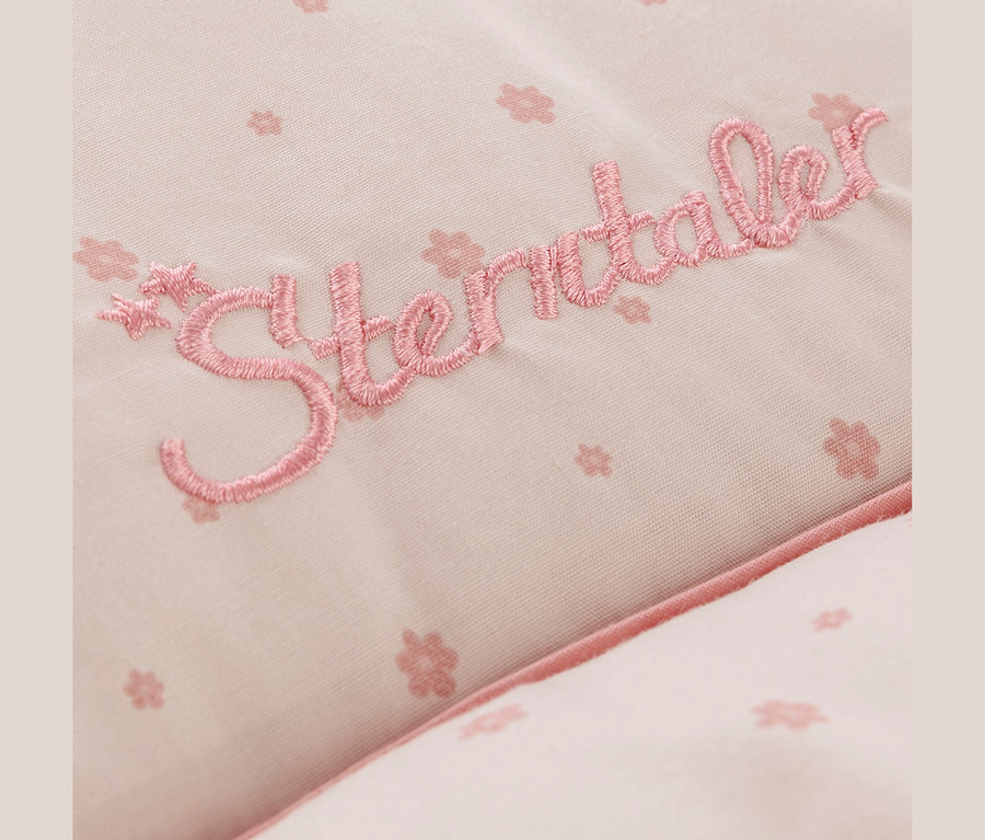 Detail svetloružovej látky s jemným kvetinovým vzorom a vyšívaným nápisom „Sterntaler“ v tmavšej ružovej farbe.