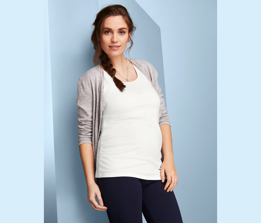Tehotná žena pózuje v bielom tope z dvojdielnej súpravy tehotenských topov a v sivom svetri.