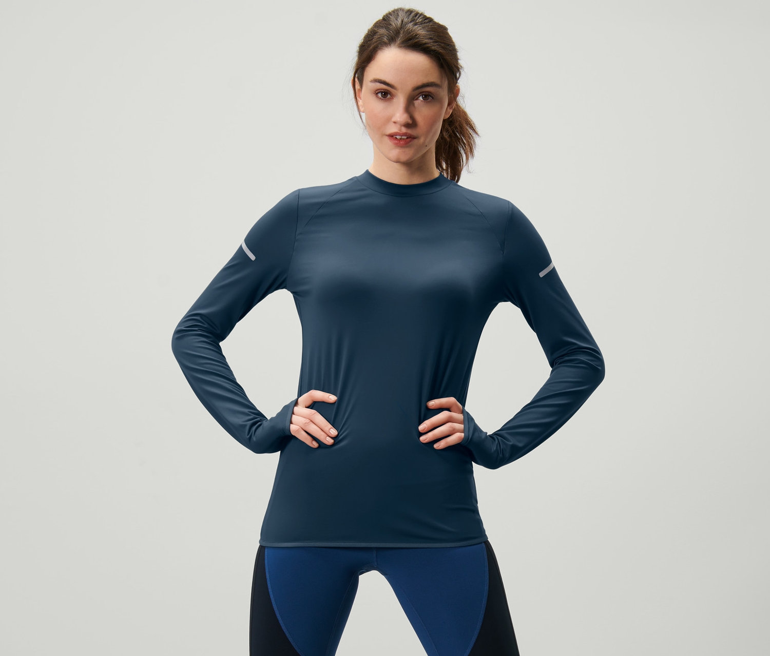 Žena pózuje v tmavomodrom funkčnom tričku s dlhými rukávmi.