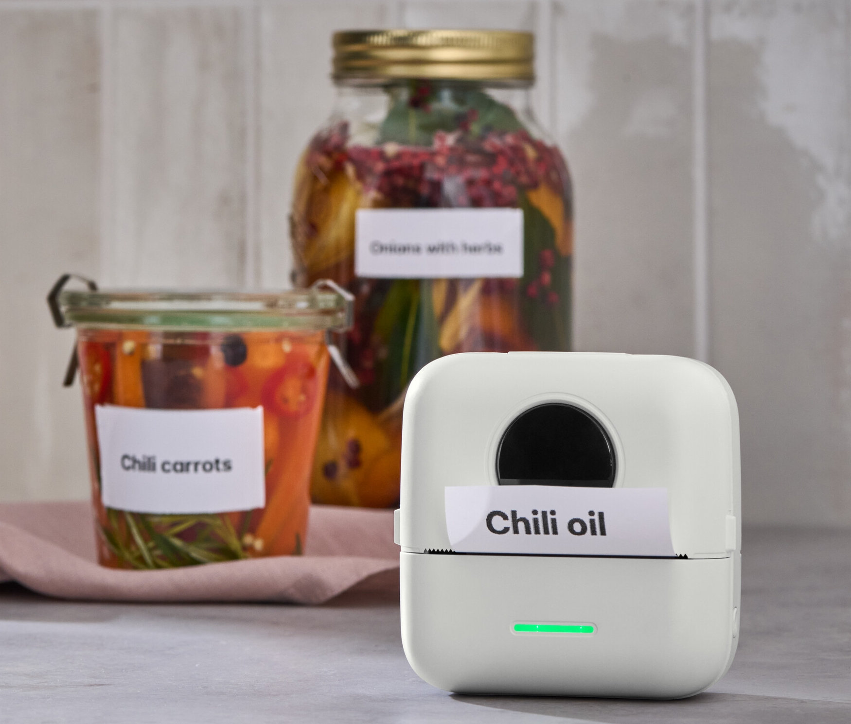 Mini termotlačiareň vytlačila štítok s nápisom Chilli oil. V pozadí poháre s chilli mrkvou.