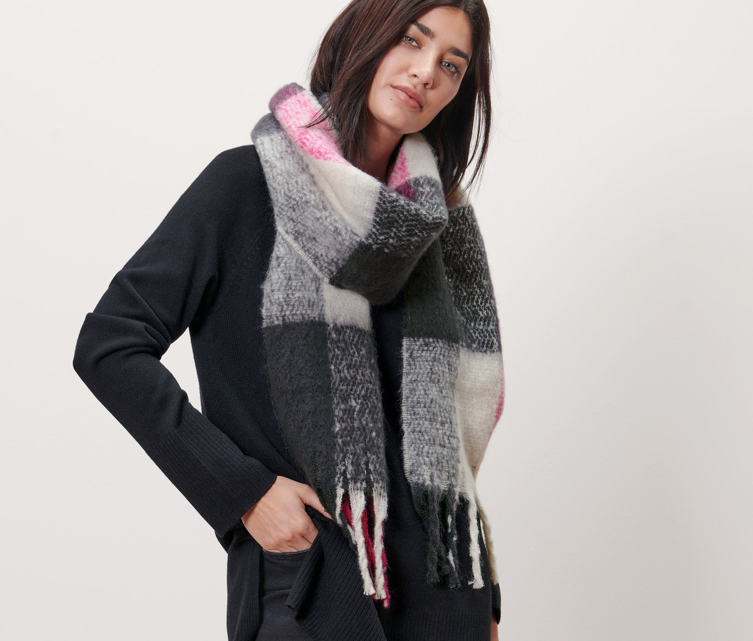 Žena pózuje s kockovaným tkaným šálom. Šál má ružové, sivé a čierne kocky.
