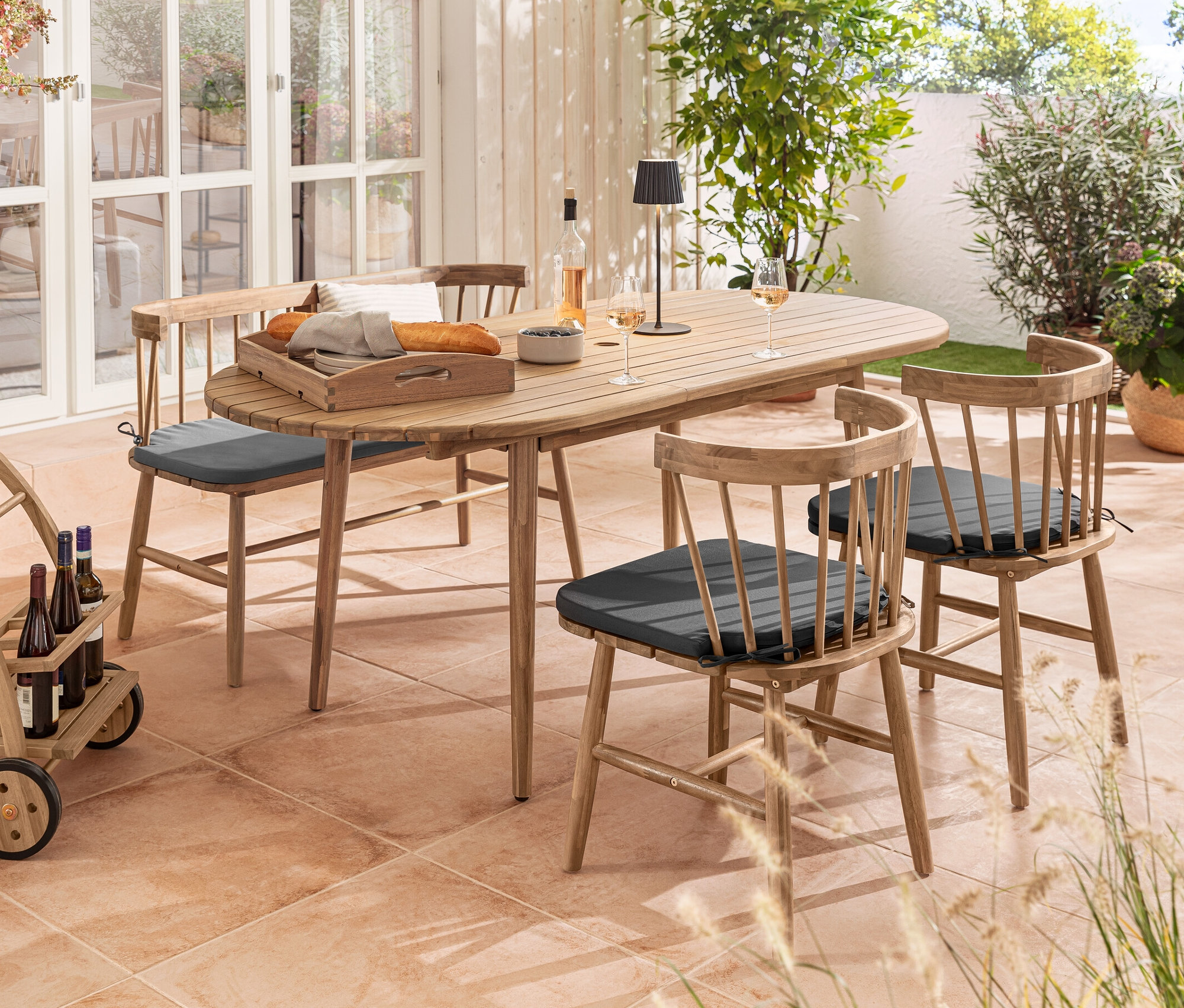 Vonkajšie sedenie s oválnym rozťahovacím stolom, obedovými stoličkami s výstelkou, lavicou s výstelkou, barovým vozíkom a čiernou LED lampou.