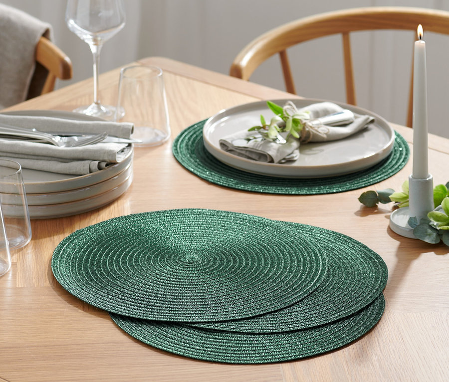 Na drevenom stole ležia 4 zelené prestierania.