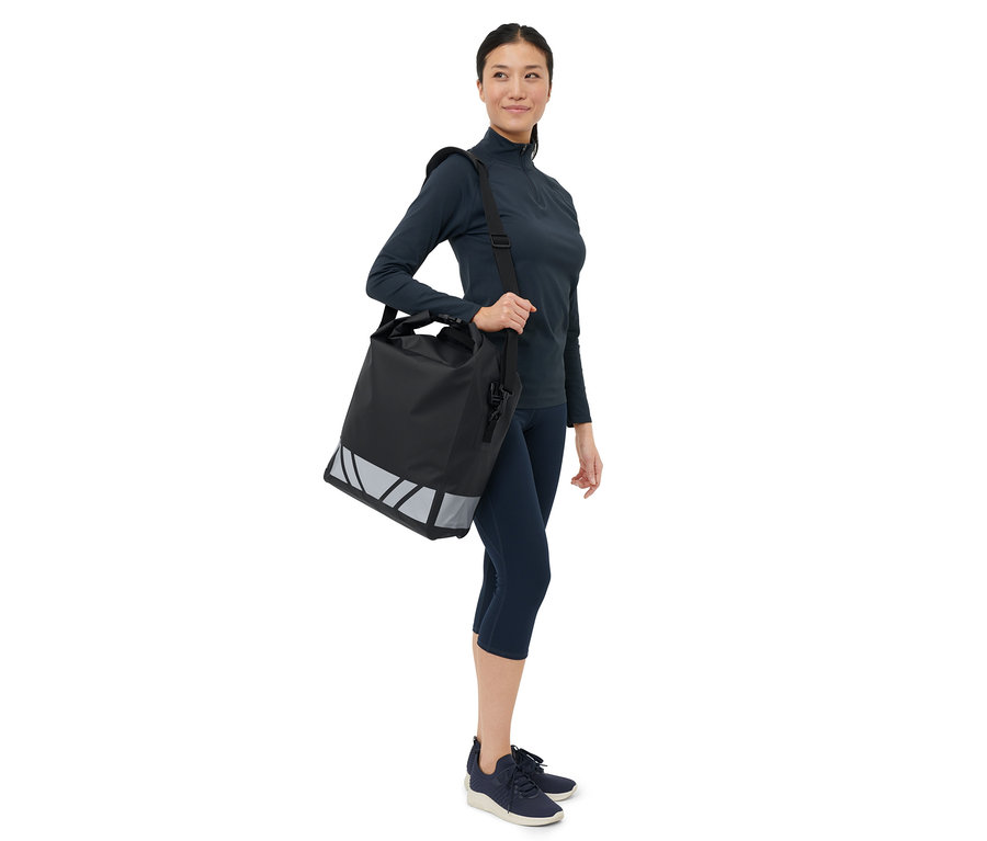 Žena nesie cez rameno čiernu vodoodolnú tašku na bicykel.