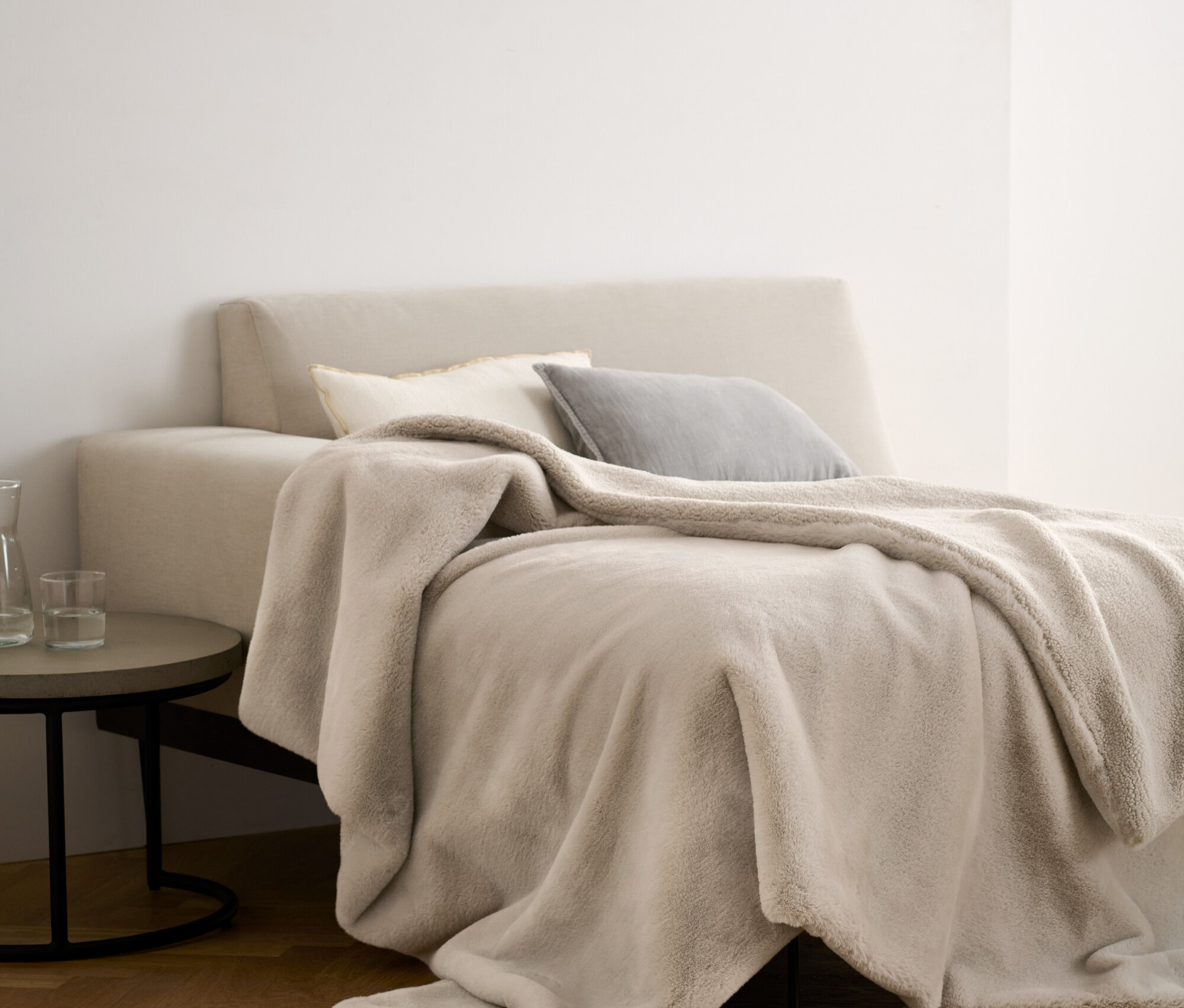 Béžová mäkučká deka z umelej kožušiny leží na posteli s vankúšmi.