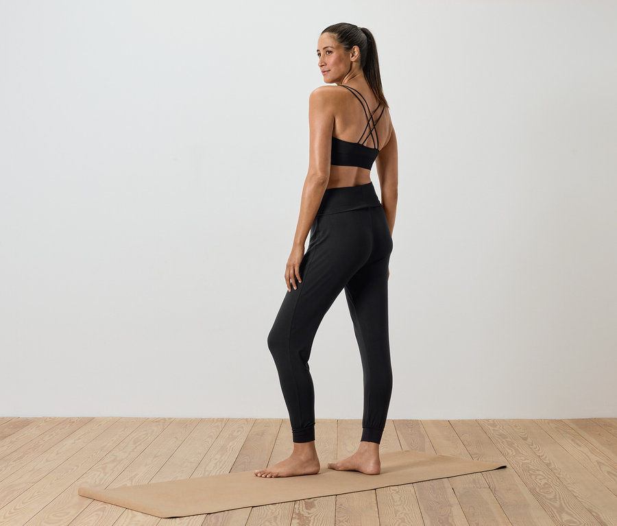 Žena v čiernom športovom oblečení stojí na podložke na cvičenie.