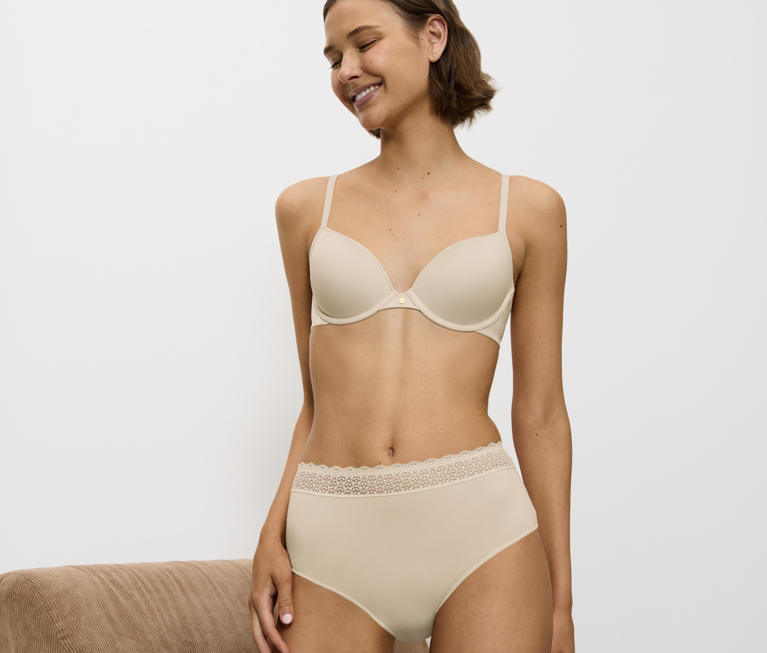 Žena sa usmieva a má na sebe béžovú podprsenku a nohavičky s čipkou.