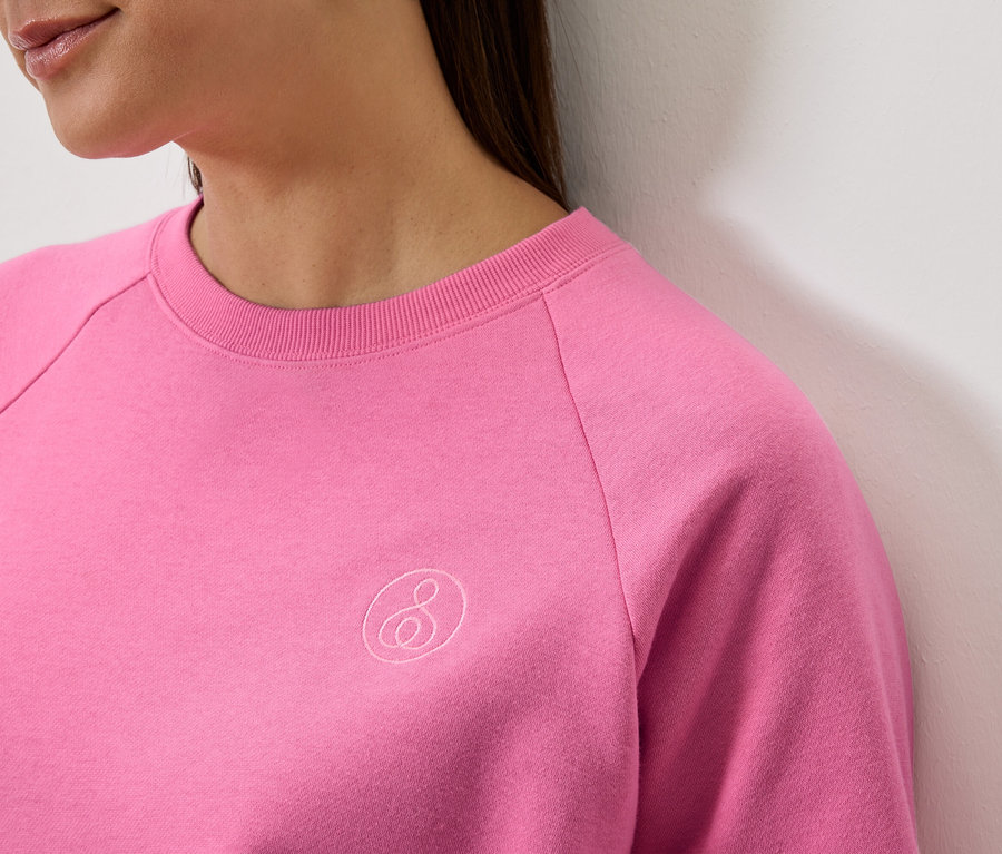 Detail ženy v ružovej mikine s dlhým rukávom s logom.