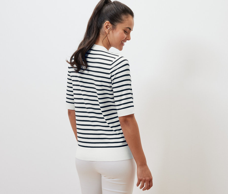 Žena stojí chrbtom a má na sebe tmavomodrý pruhovaný pulóver z jemného úpletu.